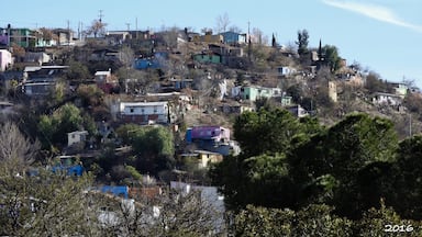 The colourful hill slopes of Nogales, Arizona, which borders the city of Nogales, Sonora, Mexico, and is Arizona's largest international border community. The highways meeting in Nogales comprise a major road intersection in the CANAMEX Corridor, connecting Canada, the United States and Mexico.