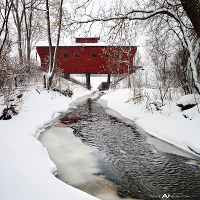 A short distance out of the small city of Milton, WI is a neat old wood covered bridge. It provides a little used road over a small meandering stream. On this Winter day we received over a foot of snow. The white flakes and the red bridge created one of my favorite Americana photos. The tree lined snowy path provides a surreal and wintery feel.