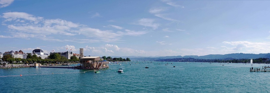 A panorama of the stunning Lake Zurich from the Quaibrucke Bridge. On a lovely summer's day there is a lot of activity on the Lake including a wooden lido with rest areas and cafe/bar.