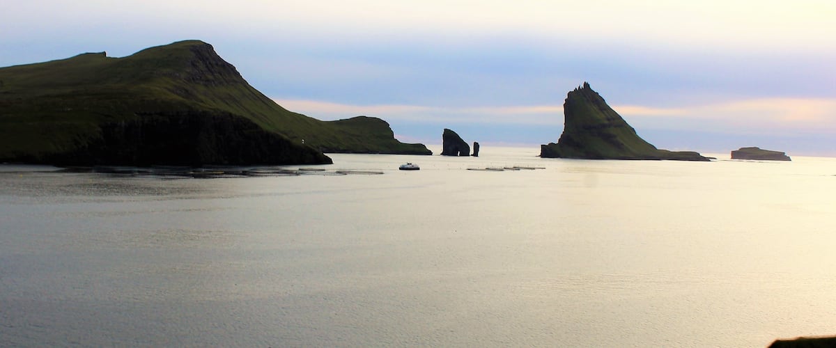 A distant view of Drangarnir, one of the most interesting natural landmarks in the Faroe Islands! Drangarnir is the sea stacks in the middle. I took this photo in/near the village of Bøur. Shortly after I visited another iconic landmark: Múlafossur Waterfall! I wish I had time to get a close-up view of Drangarnir, though. It is truly otherworldly!  
I took this photo on August 29th.