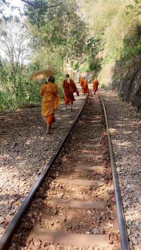Monks on the tracks of the popular tourist train line going through Kanchanaburi Province, along the Kwai river and on its famous bridge, Western Thailand.