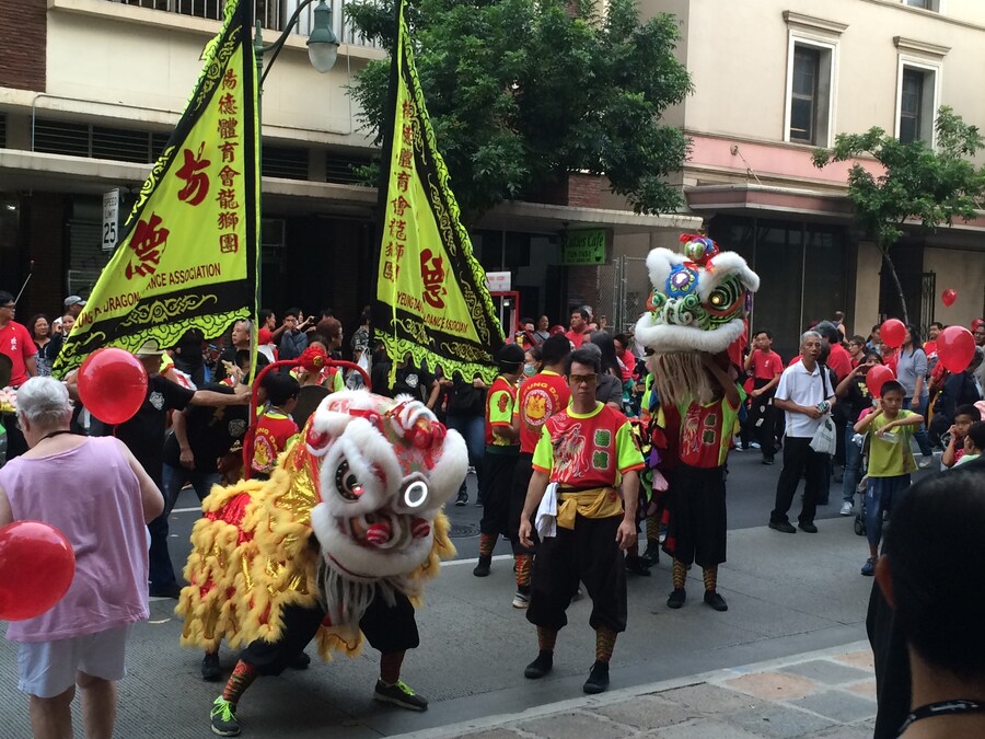 Chinatown Honolulu Lunar New Year parade with lion dance performers, bright banners, and crowds along the city street.