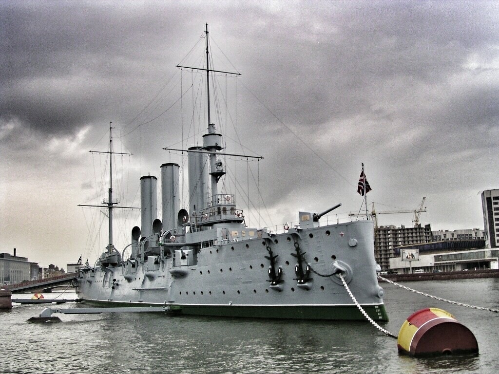 Source: Wikipedia
Aurora (Russian: Авро́ра, tr. Avrora; IPA: [ɐˈvrorə]) is a 1900 Russian protected cruiser, currently preserved as a museum ship in St. Petersburg. Aurora was one of three Pallada-class cruisers, built in St. Petersburg for service in the Pacific Far East. All three ships of this class served during the Russo-Japanese War. The Aurora survived the Battle of Tsushima and was interned under U.S. protection in the Philippines, eventually returned to the Baltic Fleet. The second ship, Pallada, was sunk by the Japanese at Port Arthur in 1904. The third ship, Diana, was interned in Saigon after the Battle of the Yellow Sea. One of the first incidents of the October Revolution in Russia took place on the cruiser Aurora.