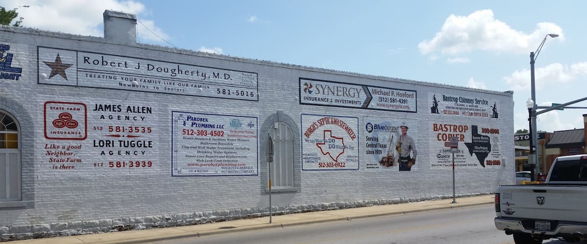 Signs painted on the side of a building at the corner of Chestnut and Main streets, Bastrop, Texas.