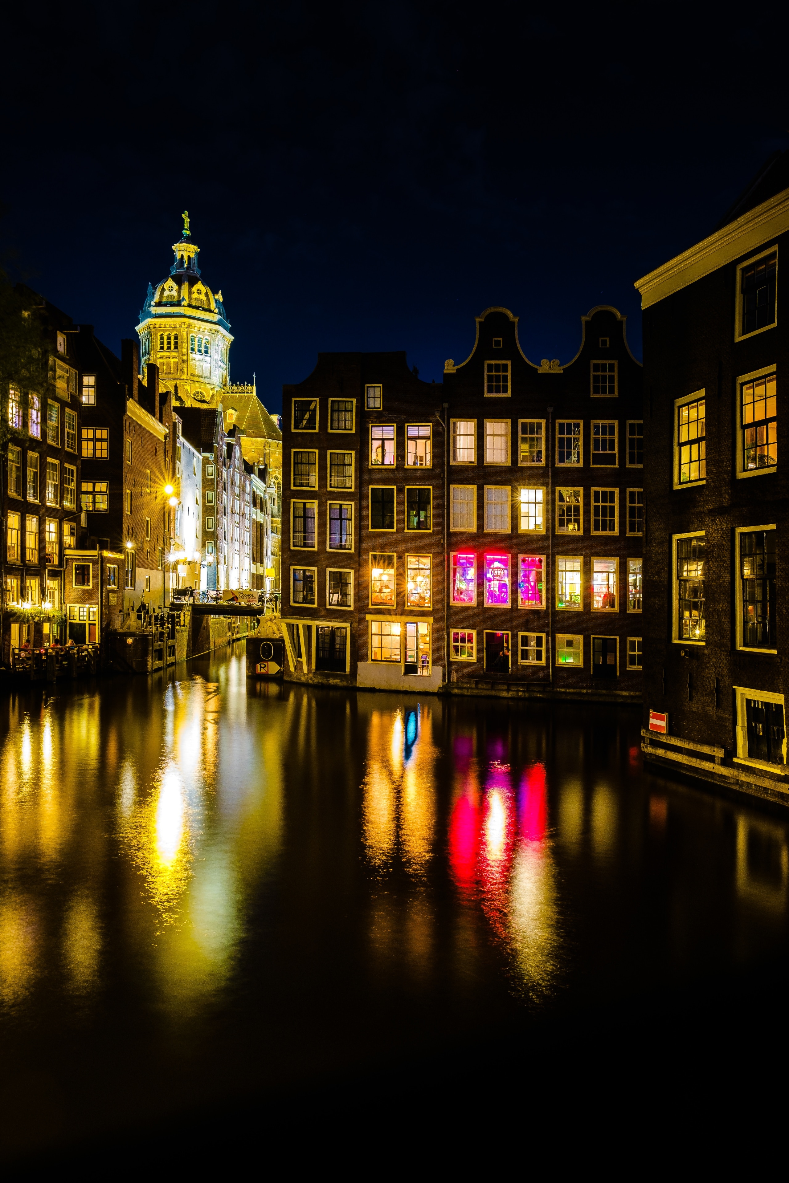 You can capture beautiful reflection shots in Amsterdam at night. In the background here the tower of the Basiliek van de Heilige Nicolaas, built between 1884 and 1887.