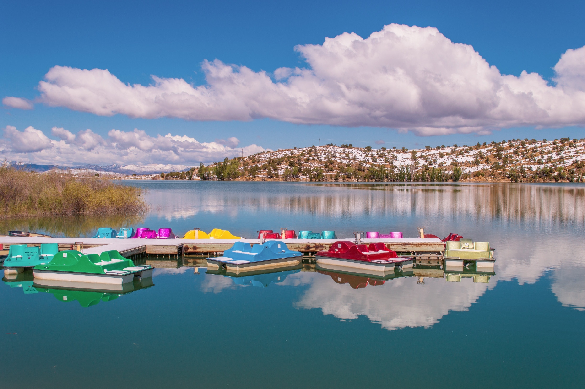 Colorful paddleboats on crystal blue Palisade Lake in Paslisade State Park. We were there in May of 2014, and woke up on Mother's Day to a surprise 9 inches of snow! It had mostly melted by the next day but still provided a pretty contrast to the bright blue sky. This state park offers fishing, camping, golfing, OHV trails, and boat rentals. #utah #palisadelake #snow #lake