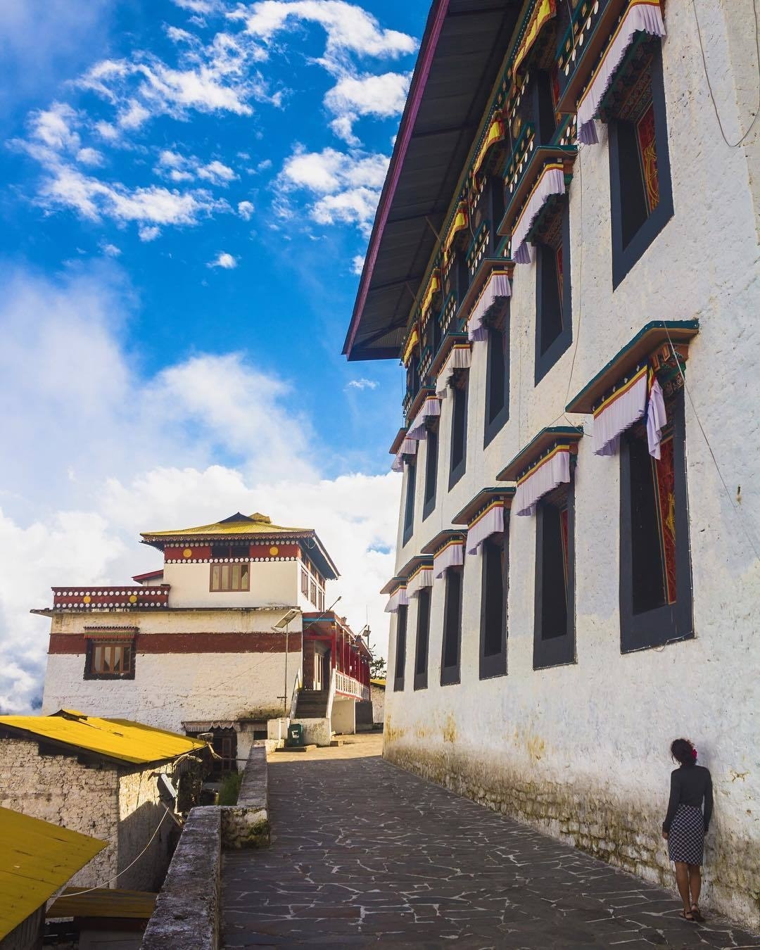 One of our favourite shots from Tawang monastery in Tawang, Arunachal Pradesh state, northeast India. 📿Tawang monastery is the largest Buddhist monastery in India and the 2nd largest in the world, only surpassed by Potala palace in Lhasa, Tibet. 💫It's a colossal, self-contained medieval citadel and built across three different levels and harbouring hundreds of resident monks.

In this image, you are observing the  approach to the main courtyard of the monastery. Jili is leaning against the whitewashed wall of the principal prayer house, which enshrines a huge Buddha statue. 

How elegant and refined those windows are! 

To the left are monks’ residential buildings with their distinctive yellow roofs. ✨That graceful edifice in the distance, situated right at the entrance to the main courtyard, is where you will find butter lamps 🔥burning inside a small room on the upper level. There is also a balcony up here where one can indulge in a magnificent panoramic view overlooking Tawang. 

We will have to show you that wonderful view another time.

⭐️So now tell us, how does this image make you feel? Is this the image that comes to your mind when somebody mentions the word India 🇮🇳? Do you think many people fail to grasp how diverse India truly is and dismiss it as a travel destination as a result?