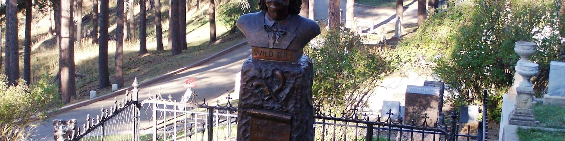 The most important event in Deadwood, South Dakota history was a poker game in Saloon #10 on August 2, 1876, where the sniveling coward Jack McCall snuck up and shot Wild Bill Hickok in the back of the head. Hickok had arrived in Deadwood only a few weeks earlier, played a succession of card games, and never in his life sat with his back to the door. Until that day. 
Above the town, on a ridge, tourists can visit the graves of Wild Bill and Calamity Jane in Mount Moriah Cemetery.