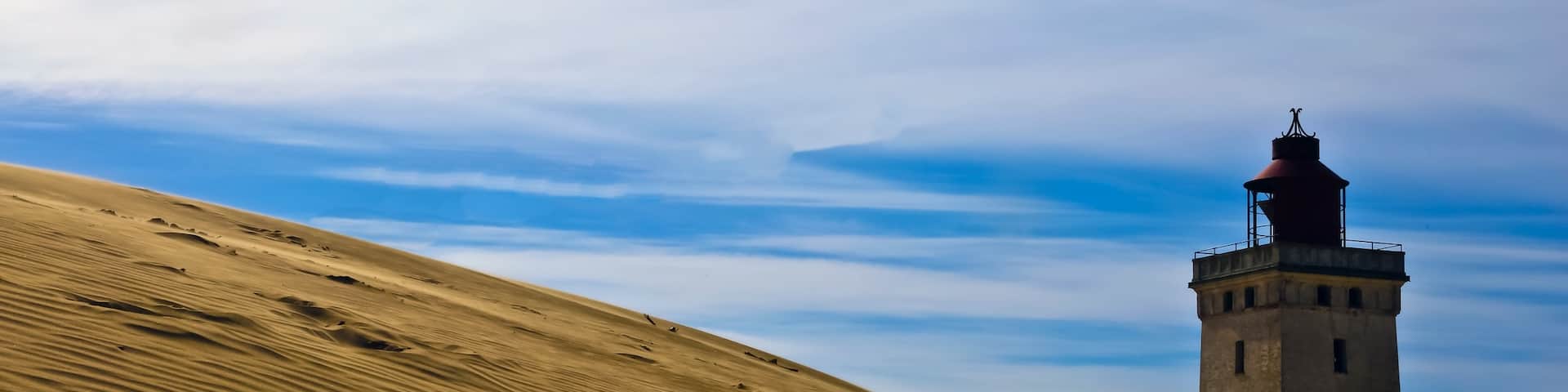 Welcome to Denmark !!
This is Rubjerg Knudle Lighthouse near Aalborg on the Northwestern coast of the North Sea. It was first lite in 1900 and was functional to 1969.
The interior (somewhat unsafe brick and stairs) will be closed in a year and the entire structure is expected to be swallowed by the sea within 10 years. It was officially closed as a Lighthouse in 1969 and later in 1980 re opened as a giant Kaleidoscope.
The 3 supporting houses next to the lighthouse have already been destroyed by the encroaching sea and deepening sand dunes.
This will be a casually of global warming and the encroachment of the sea.