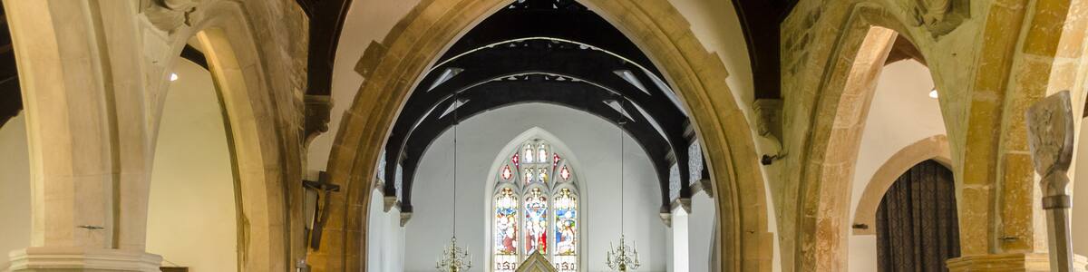 Photo "St Mary's at East Barkwith is one of 6 parish churches of the united Parish of the Barkwith Group. The church has undergone several rebuildings, so the present structure is a combination of different styles. There is no record of when the first church was built here, or of its appearance. The Domesday Survey of 1086 records a church at Barkwith, but it is not known of it was on this site or at West Barkwith. The earliest parts of the church date from between 12th and 13th C onwards, and subsequent dating may be determined by the style of the architecture, Perpendicular, which may be seen in the entrance door and porch, the archway to the tower and the tower itself. The west window may have been reused from an earlier building and the bell openings in the upper tower were probably made in the 17th century. The south arcade also dates from the Perpendicular period. This part of the church saw Catholic services in the centuries before Henry VIII, then changed between Catholicism and Protestantism under Edward, Mary and Elizabeth, the introduction of the Book of Common Prayer (1549, 1552 and 1662), and the destruction of the religious statues and stained glass under the Puritans. In the 18th century there was a long period of neglect and decay in the Church of England. Nonconformist churches began to develop and split from the Anglican church, which suddently took fright and began to appoint incumbents and repair churches. At St Mary's, the chancel was rebuilt in 1846, the architect being J.B. Atkinson. In 1868/9 the nave was re-roofed; the north aisle, the arcade and the windows were rebuilt under the direction of R.J. Withers. The difference in colour and tooling between the original pillars and the 19th century pillars are quite obvious. The font dates probably from the 15th C. It is octagonal and is decorated with shields bearing nails, whip, crown of thorns and other instruments of Christ's Passion. The font is lead lined, and drains through the stem to the ground beneath, so that the hallowed water could not be taken for superstitious purposes. As the water was sometimes left in the bowl the lid could be fastened down; the marks where the hasp and padlock would have been can still be seen on the font. The pulpit is unusual, being made of metal, and was designed by Christopher Turnor of Panton Hall in the late 19thC." by Jules & Jenny (Creative Commons Attribution 2.0) / Cropped from original