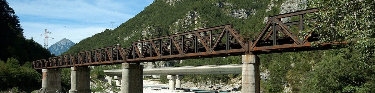 Photo "Railroad bridge across the river Fella, part of a defunct railroad line called the old "Pontebbana", in the north-eastern part of Italy, region Friuli Venezia-Giulia. In the background there are the two bridges of the Autostrada Alpe-Adria." by Johann Jaritz (Creative Commons Attribution-Share Alike 3.0) / Cropped from original