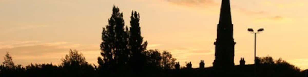 Photo "Sunrise over Failsworth, in Greater Manchester, England. The steeple is of St John the Evangelist's parish church. The waters are that of the Rochdale Canal." by Martin Butler (Creative Commons Attribution-Share Alike 2.0) / Cropped from original