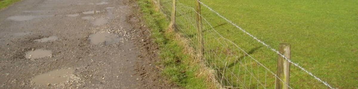 Photo "Lodge Hill, near Bracewell, Yorkshire. Lodge Hill is a low rounded hill and is a 'drumlin', of which there are many in this area. Beyond it is seen a woodland known as Big Covert, while in the dip between the hill and the wood is a fishing lake. Photograph taken on a rainy April morning, with sheep and lambs in the adjoining field." by Dr Neil Clifton (Creative Commons Attribution-Share Alike 2.0) / Cropped from original
