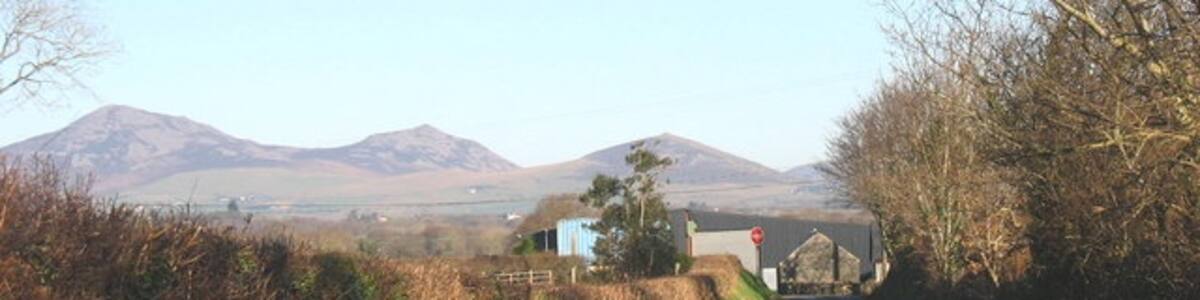 Photo "Approaching the junction with the B4415 at Llwyn Beuno The Eifl hills form the background," by Eric Jones (Creative Commons Attribution-Share Alike 2.0) / Cropped from original