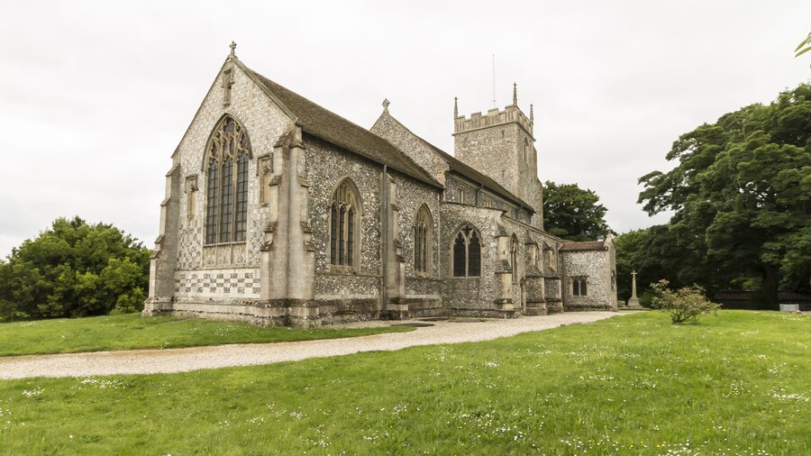 Photo "The church consists of a west tower, four-bay nave and aisles, chancel, and a north porch. The three stage tower was originally built in the early 15th century, but partly fell in the early 19th century and was probably reduced in height at that time. There is a battlemented parapet with crocketted pinnacles and gargoyles. It is decorated with Shields and panels of black flints. The nave has 13th century north and south arcades of four bays, with round piers and seat bases. There is a small perpendicular clerestory. There is a rood beam with a rood. The chancel has a finely decorated exterior east wall with checker patterns and three (empty) niches. There are also several mass dials. The chancel has a 15th century canopy over its piscina and sedilia. The north east end of the nave originally had a Chapel, There is a squint, a tomb slab from circa 1300 and a wall recess. In the centre of the chancel floor is a large brass to Sir William Calthorpe, died 1420. Burnham Thorpe is famous for being the birthplace of Lord Nelson, and he was baptised in the church. There are several references to him in the church. The lectern is made from a beam from HMS victory, given by Lords of the Admiralty in 1881. There is also a bust of Nelson and a Memorial for his father who was rector at the church and died in 1802. The church was renovated for the centenary of the Battle of Trafalgar in 1905. There is a Purbeck marble font dating from the 13th century with pointed arches on the faces. There is a small but fine organ which is currently the earliest survival by maker Samuel Street. Pic by Jenny." by Jules & Jenny (Creative Commons Attribution 2.0) / Cropped from original