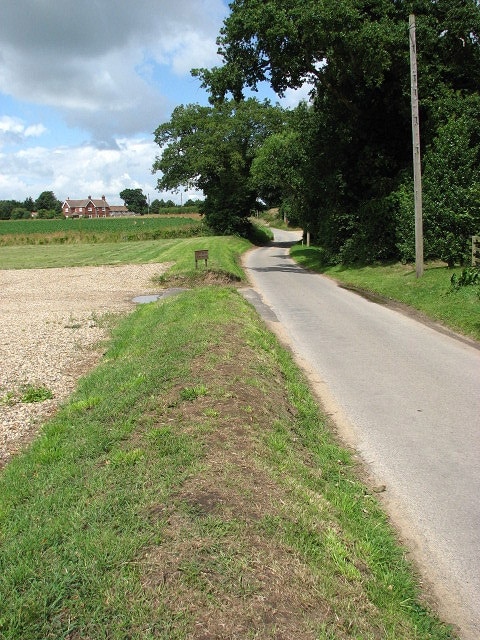 Sweetbriar Lane. Past Church Farm > 876024 and the church of SS Peter and Paul > 876028. Part of the church car park can be seen at left. The view is westerly; the red brick house seen in mid-distance at left is the Old White Horse > 543873.