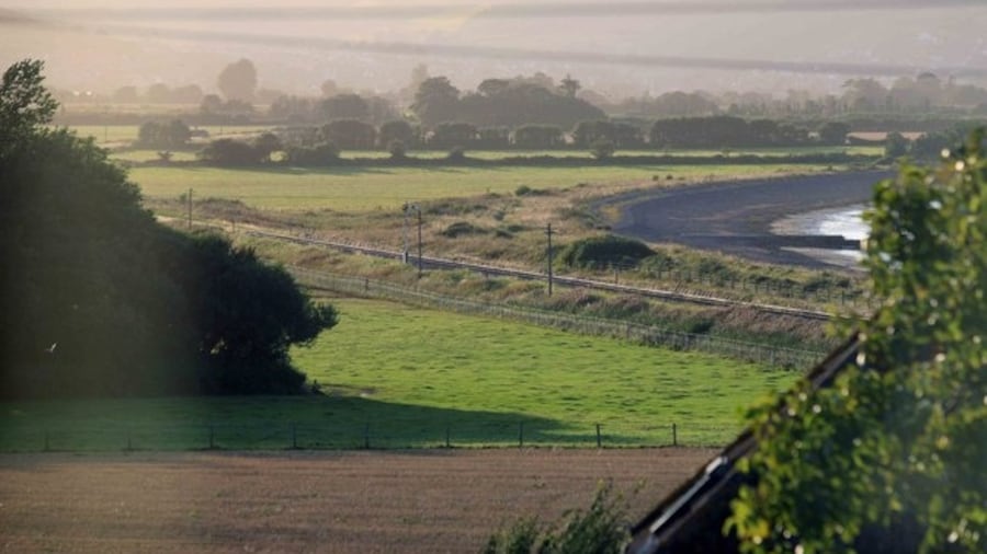 Photo "Evening view Looking towards the Blue Anchor bay and the hills. The West Somerset Railway can be seen in the foreground with the sea just visible. In the distance are the hills, hazy as the camera is looking towards the setting sun." by roger geach (Creative Commons Attribution-Share Alike 2.0) / Cropped from original