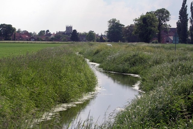 Drainage ditch beside a road at Great Hale, Lincolnshire, with the tower of St John the Baptist's parish church in the background