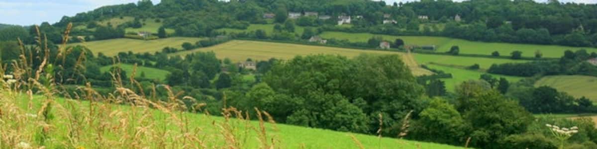 Photo "View from Shockerwick Lane Through a gap in the hedgerow on Shockerwick Lane we can look east up the valley of the By Brook toward Box. The hill to the right is Kings Down with its golf course and clinging to the near side we can see upper part of Kingsdown village." by Maurice Pullin (Creative Commons Attribution-Share Alike 2.0) / Cropped from original