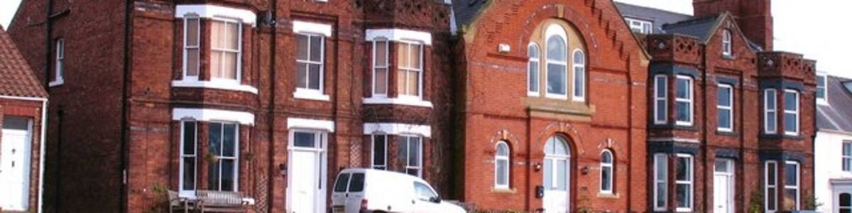 Photo "Houses at Middleton One Row A curious group of houses in Middleton. The central section looks as though it should have been a chapel, whilst the 'wings' are of a different brick. Maybe a visitor to the website can throw some light on the history of this block." by Gordon Hatton (Creative Commons Attribution-Share Alike 2.0) / Cropped from original