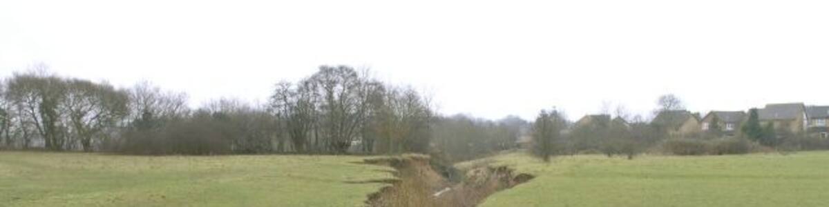 Photo "A brook cuts into a field near Borough Green. At one end of this field near Borough Green, the brook is just a trickle and the footbridge (just off picture) isn't really needed but by the time the stream reaches the other side of the field it has cut a gorge 10 metres wide revealing pipes and other subterranean structures. This picture doesn't really convey the visual impact of this strange scar in the middle of what would otherwise look like a normal field." by Hywel Williams (Creative Commons Attribution-Share Alike 2.0) / Cropped from original
