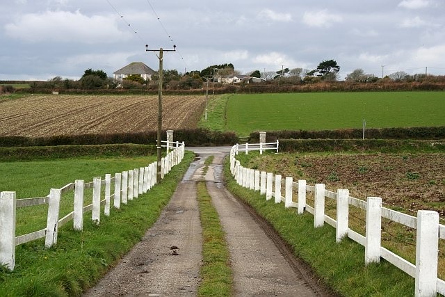 Footpath across the main road. The footpath follows the farm entrance road then crosses the A394 and onto rough grass between the fields. Almost all the signposts to this footpath have been turned around to point in a misleading direction. This is quite a common act of vandalism in rural areas.