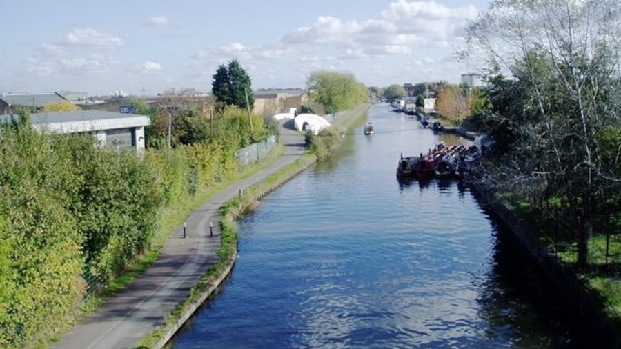 Photo "Grand Union canal showing the Bulls Bridge. View from The Parkway looking east. The Bulls Bridge is the white structure on the left of the canal in the middle distance. Tesco supermarket is to the right (unseen). The partially revealed square structure on the left is part of the Volvo truck servicing centre." by J Taylor (Creative Commons Attribution-Share Alike 2.0) / Cropped from original