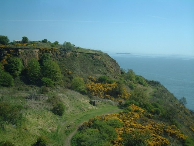 Fife Coastal Path. The line of the Coastal Path between the Firth of Forth and the disused quarry workings at North Queensferry. Photographed from a train approaching the Forth Bridge.