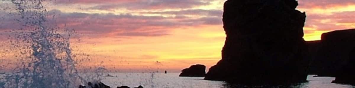 Photo "Marsden Sploosh At Dawn Wave hits rock with limestone stack in the distance. Just after sunrise, June 2006." by John Harvey (Creative Commons Attribution-Share Alike 2.0) / Cropped from original