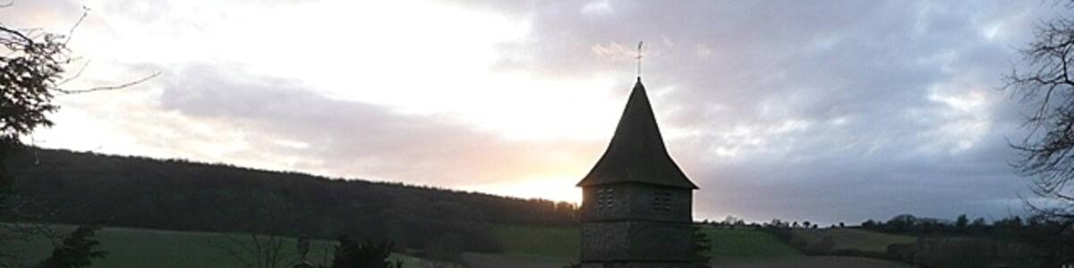Photo "St. Peter's church, Hurstbourne Tarrant The north side from the steeply rising churchyard with the sun setting over Wallop Hill Down behind. The 17th century clerestory roof is clearly seen from this angle, as is the 15th century three-stage weatherboarded bell tower. There is more information here http://www.astoft.co.uk/hurstbourne.htm" by Graham Horn (Creative Commons Attribution-Share Alike 2.0) / Cropped from original