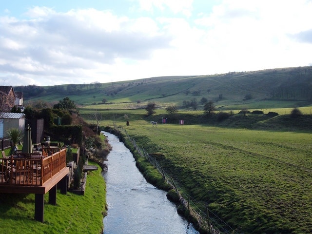 River Beal, Newhey Looking south from the bridge at the end of Bentgate Street. The rear gardens of houses on Whitebeam Close have been extended onto the river bank. The houses on the east bank are in Rochdale whilst the grazing land on the west bank is in Oldham. The ridge on the skyline carries the Rochdale Way, the Oldham Way and the Crompton Circuit footpaths.