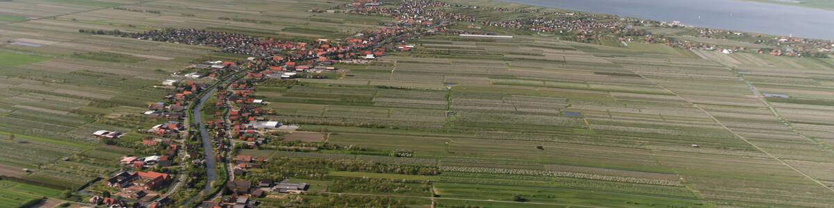 Photo "Luftaufnahme: der kleine Fluss, an der linken Bildseite, ist die Lühe, der Ort links ist Steinkirchen, der Ort rechts ist Mittelnkirchen, der Ort vor der Elbe ist Grünendeich, in der Elbe dahinter liegt der Lühesand" by Walter Rademacher (Creative Commons Attribution-Share Alike 3.0) / Cropped from original
