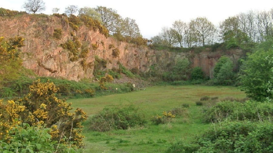 Photo "Morley Quarry, Shepshed, looking south. Charnwood Borough Council acquired this site, ostensibly to equip for climbing. Although it isn't actually much good for climbing, it does show the outline of a wadi (desert stream) bed infilled with Triassic-Rhaetic marls at the top of the southern face. The eastern face, seen here, reveals northward sloping Charnwood volcanics of Precambrian age. The quarry would have been built to excavate one of the many syenite intrusions in Charnwood Forest." by Sue Hutton (Creative Commons Attribution-Share Alike 2.0) / Cropped from original