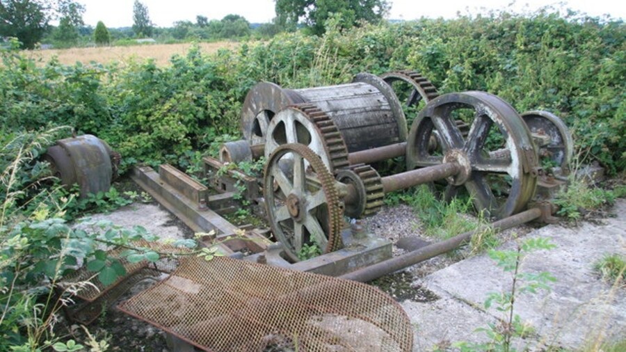 Photo "Remains of converted steam winch, Swannington This is at the top of the Swannington Incline and appears to have been relocated here. It was once a double reduction geared twin cylinder steam winch. One disc crank has been replaced by a gear and there is a loose electric motor and chain guard that presumably went with it. The engine has Easton & Tattersall, Leeds cast in the bed - a maker I'm not familiar with." by Chris Allen (Creative Commons Attribution-Share Alike 2.0) / Cropped from original