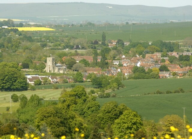 West Lavington from Strawberry Hill 452274 gives a view of West Lavington from a different direction. 'It lies far away from the coming and going of the great busy world,' wrote an inhabitant in 1875. Today, and for many decades, the great busy world speeds along the A360 from Salisbury to Devizes and threads its way precipitously through the chicane formed by the churchyard and the almshouses. In fact the main road spends about 8km in West Lavington parish, from the high downland south of Gore, the 'buried village of Salisbury Plain', past Gore Cross, where it is intersected by an important ridgeway, down a long descent beside landscaped woodland (known as The Warren) and into the pleasant valley where the village sits, then along some 2km of ribbon development associated with the linear village of Littleton Pannell, before leaving the parish north of the railway bridge. This journey is familiar to most Wiltshire travellers, and even without realising that chalk is giving way to Greensand and clay, many must feel as they pass along that here south Wiltshire ends and west Wiltshire begins" All this and more in: http://www.wiltshire.gov.uk/community/getconcise.php?id=237