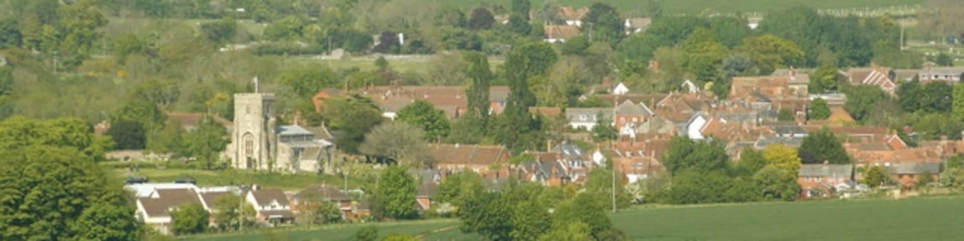 West Lavington from Strawberry Hill 452274 gives a view of West Lavington from a different direction. 'It lies far away from the coming and going of the great busy world,' wrote an inhabitant in 1875. Today, and for many decades, the great busy world speeds along the A360 from Salisbury to Devizes and threads its way precipitously through the chicane formed by the churchyard and the almshouses. In fact the main road spends about 8km in West Lavington parish, from the high downland south of Gore, the 'buried village of Salisbury Plain', past Gore Cross, where it is intersected by an important ridgeway, down a long descent beside landscaped woodland (known as The Warren) and into the pleasant valley where the village sits, then along some 2km of ribbon development associated with the linear village of Littleton Pannell, before leaving the parish north of the railway bridge. This journey is familiar to most Wiltshire travellers, and even without realising that chalk is giving way to Greensand and clay, many must feel as they pass along that here south Wiltshire ends and west Wiltshire begins" All this and more in: http://www.wiltshire.gov.uk/community/getconcise.php?id=237