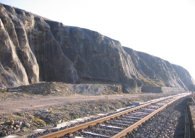 Looking Towards Parton. At first glance you may think the cliffs are a shiny light rock, they are covered in a strong wire mesh and strong wire rope to aid stability and help keep rocks off the railway.