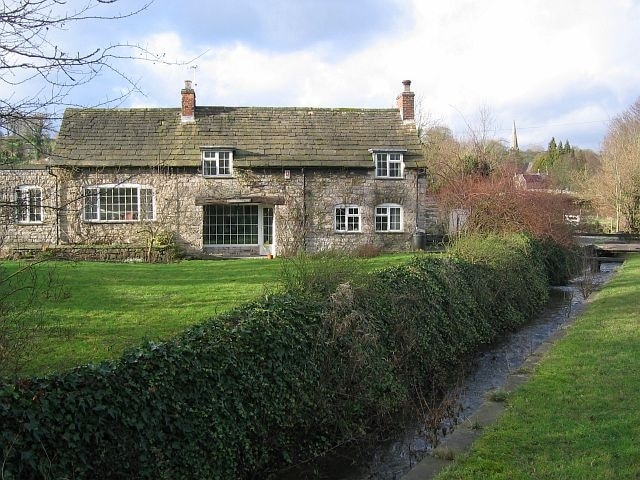 Brookside Cottage, Fenny Bentley Bentley Brook runs parallel to the Buxton-Ashbourne Road. Stone footbridges span the gap between the road and the houses. The spire of the Church of St Edmund can just be seen.