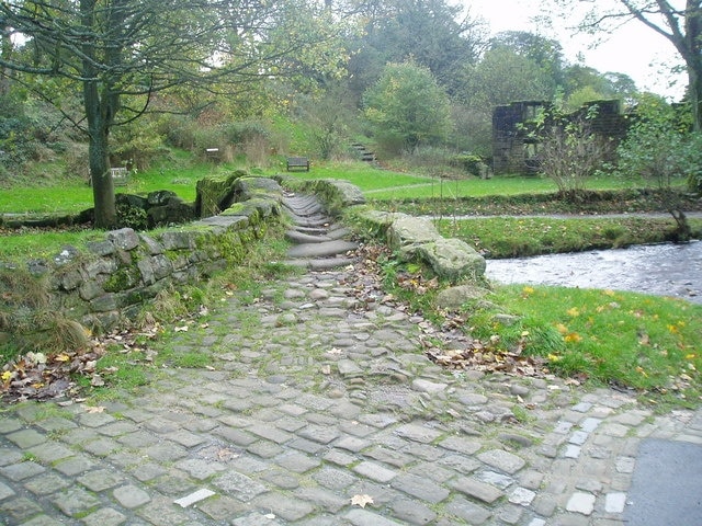 Packhorse bridge across Wycoller Beck in Wycoller, Lancashire. Beyond is part of the ruin of Wycoller Hall.