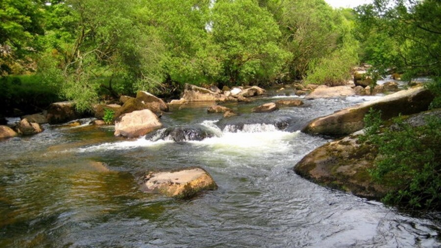 Photo "The Dart near Hexworthy Bridge It is difficult to imagine that these boulder-strewn swirling waters rush into a slow moving pool of calm before they reach the bridge." by Sarah Smith (Creative Commons Attribution-Share Alike 2.0) / Cropped from original