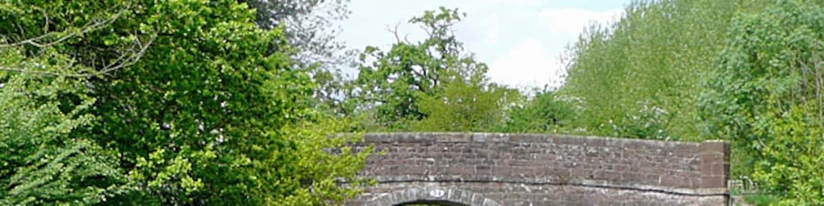 Photo "Bridge No 54, near Cheswardine, Shropshire. Westcottmill Bridge on the Shropshire Union Canal. The bridge is purely for farmers' access and a public footpath from the double bend on Westcott Lane on the left to Cheswardine on the right (1200 metres) where the Red Lion pub with its own microbrewery can be found. N.B. The footpath no longer goes through Westcott Mill Farm, but instead follows the concrete road adjacent to the canal." by Roger Kidd (Creative Commons Attribution-Share Alike 2.0) / Cropped from original