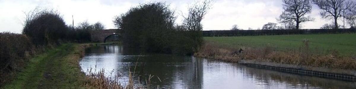 Photo "Ashby Canal near Congerstone. Looking West along the canal to Fairfield Bridge in the distance. This part of Leicestershire is generally flat apart from a few gentle undulations and the canal has no locks along its entire length." by Tony Teperek (Creative Commons Attribution-Share Alike 2.0) / Cropped from original