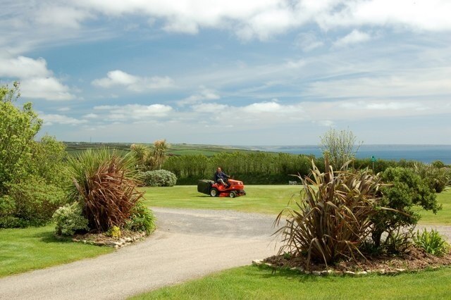 Mowing the lawn at Kenneggy Cove Holiday Park Here's Mark Garthwaite keeping his grass in tip-top nick, ready for all those campers to poke holes in it with their tent pegs and awning spikes !! In the middle background you can just see Porthleven Sands, and the Western side of the Lizard Peninsula, visible across a sparklingly clear Mount's Bay.