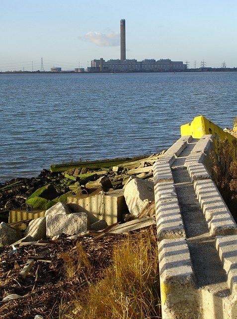 Grain Power Station from Queenborough. The footpath along the seawall veers inland at this point and a high fence (the stripy shadow) keeps you off the foreshore. Older maps show this area as below high-water mark, the reclaimed land is used for the storage of 109685 imported via Sheerness docks.