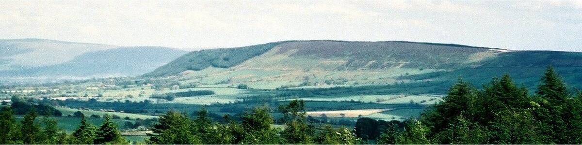 Photo "The east end of Longridge Fell, in Lancashire, England. Behind and to the left is Pendle Hill. Photographed from Beacon Fell." by Dr Greg (Creative Commons Attribution 3.0) / Cropped from original