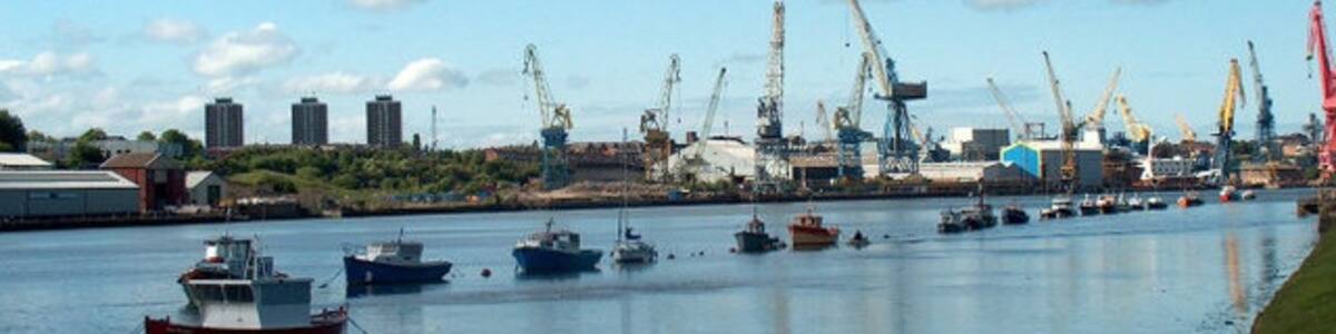 Photo "Hebburn Riverside Looking downriver from near the Bill Quay bend (behind the camera) with the cranes of Swan Hunter shipyard, Wallsend on the opposite bank. Sadly this great yard ceased operation in 2006 and the iconic cranes were sold in early 2007." by Mike Ellison (Creative Commons Attribution-Share Alike 2.0) / Cropped from original