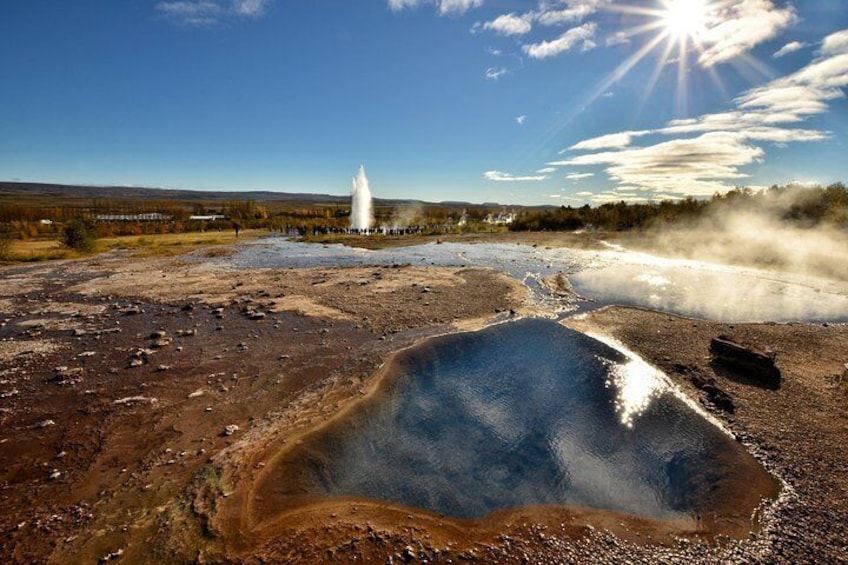 Hot spring with erupting geyser in the background