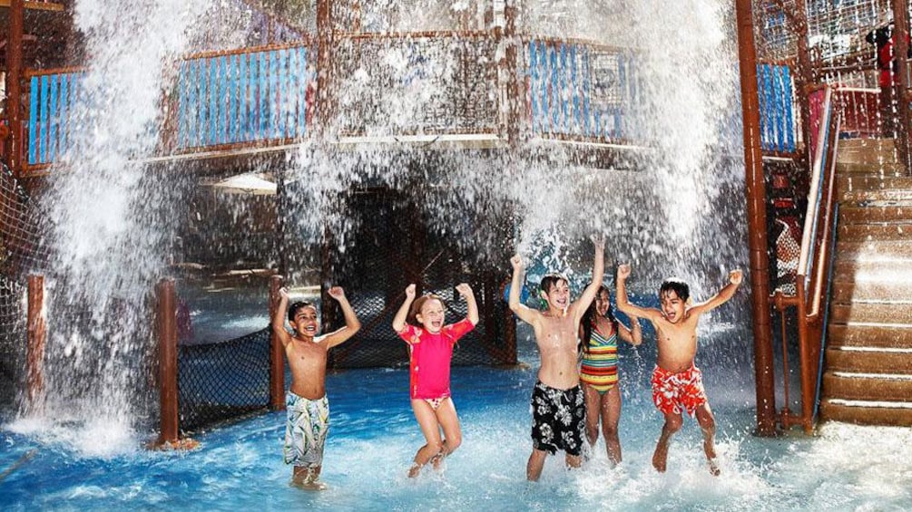 five kids laying underneath waterfall at waterpark in Dubai
