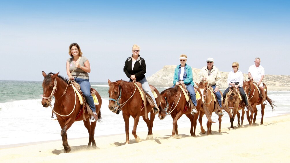 line of horseback riders on beach in Los Cabos