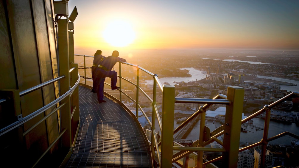Guests on the Skywalk at the Sydney Tower Eye take a break standing on a platform overlooking the city in Sydney as the sun is setting